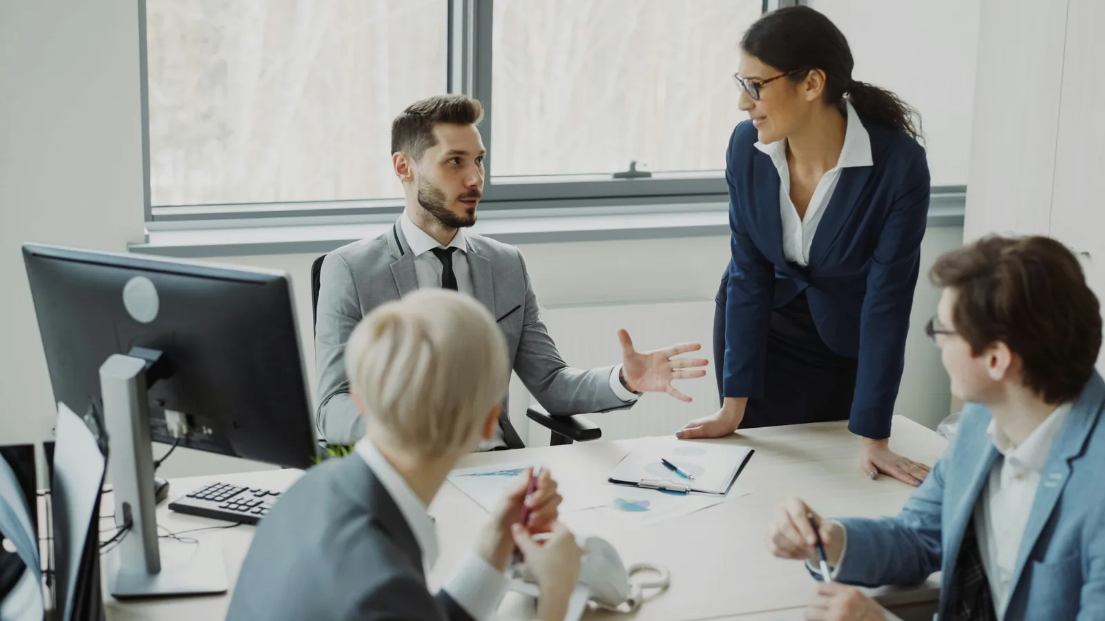 A consultant stands at a conference table talking through a plan with a seated team of three.